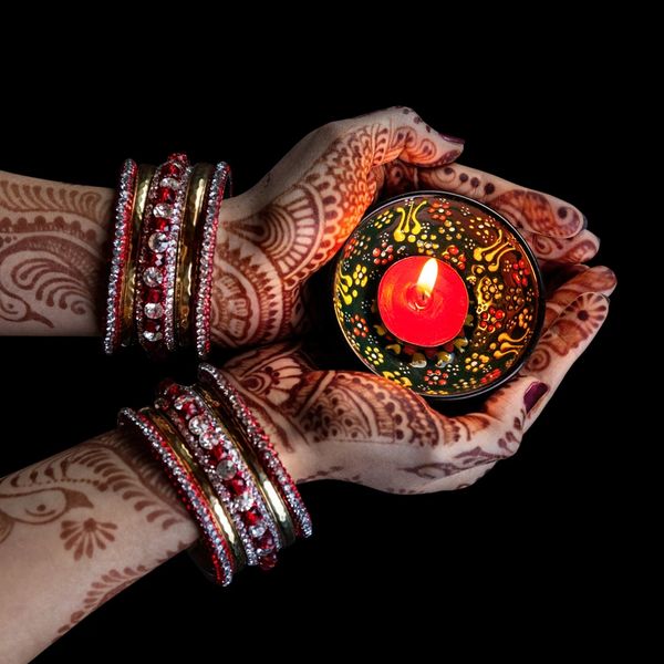 Hands adorned with mehndi and bangles holding a lit decorative candle.