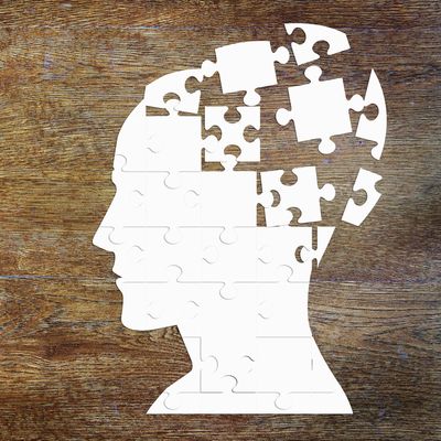 White puzzle pieces form a human head silhouette with missing pieces on a wooden background.