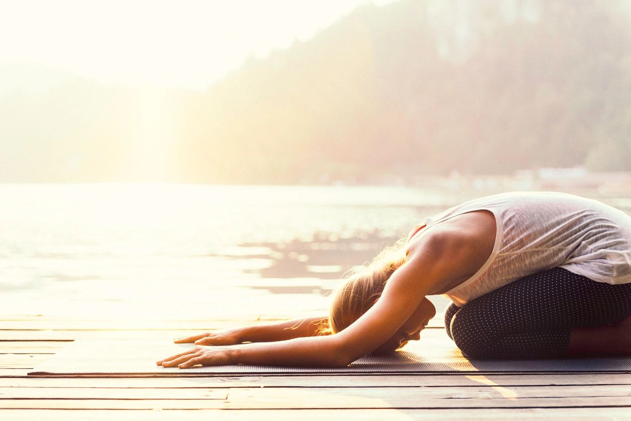 Yoga student in Child Pose on her mat near the ocean. 