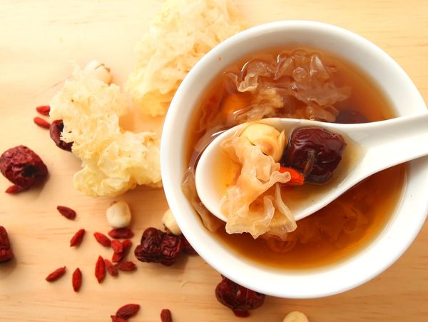 bowl of Chinese soup containing mushrooms, dates, and goji berries surrounded by dried herbs