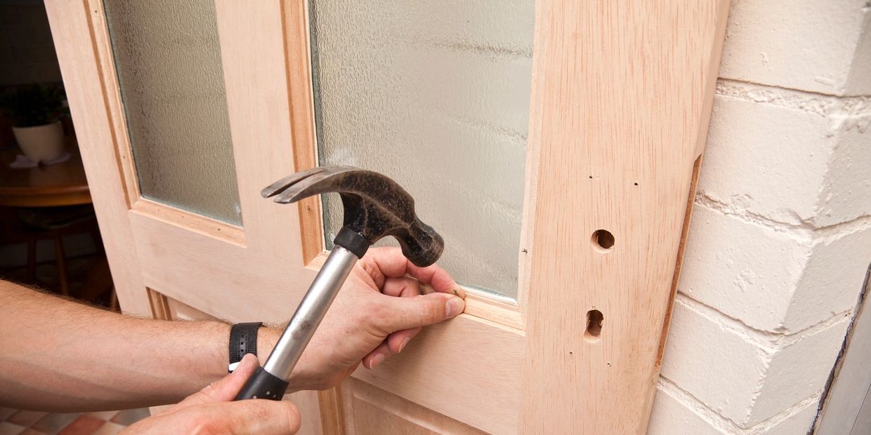 Person using a hammer to work on a wooden door near a brick wall.