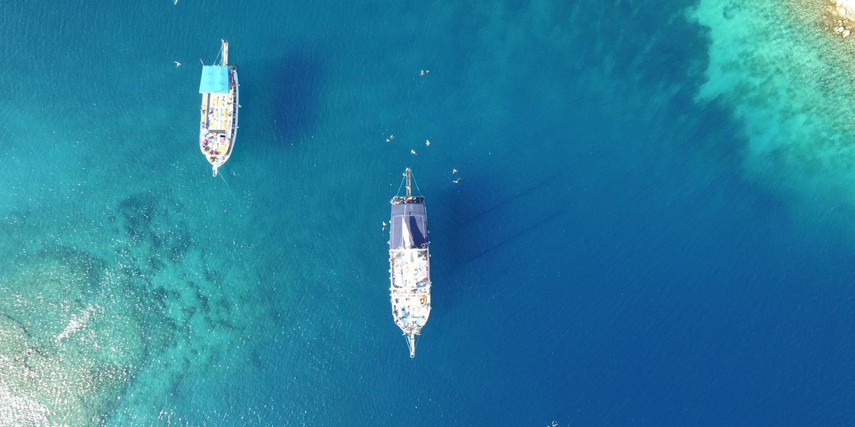 Two boats floating on clear blue water near a reef.