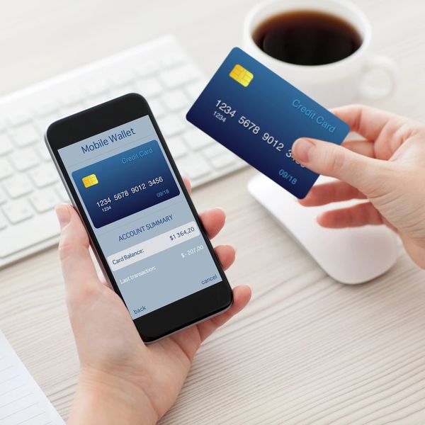 Person holding a credit card and a phone showing a mobile wallet app with account summary.