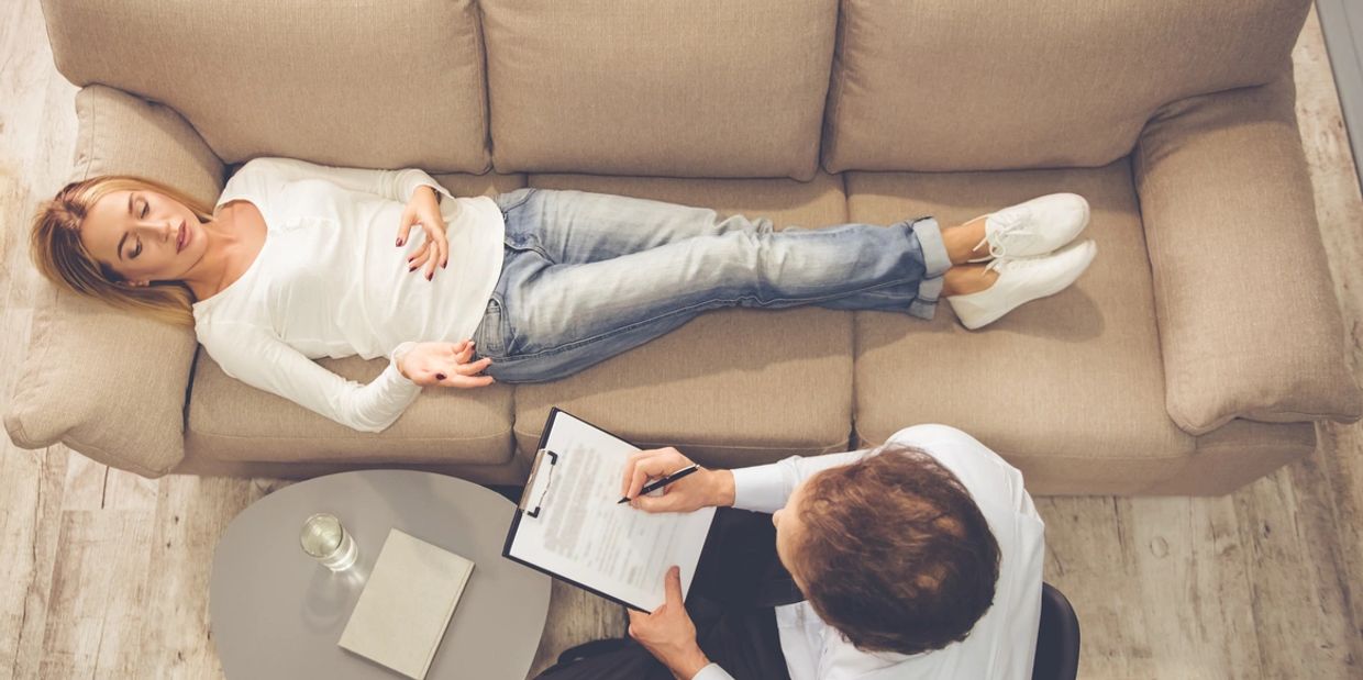 A woman lies on a couch during a therapy session with a male psychologist.