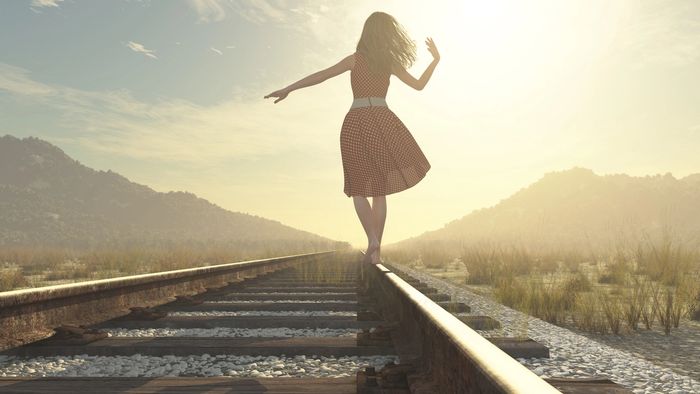 A woman in a red polka dot dress balances on a railroad tie. 