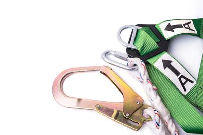 Green safety harness with metal hooks and clips on a white background.