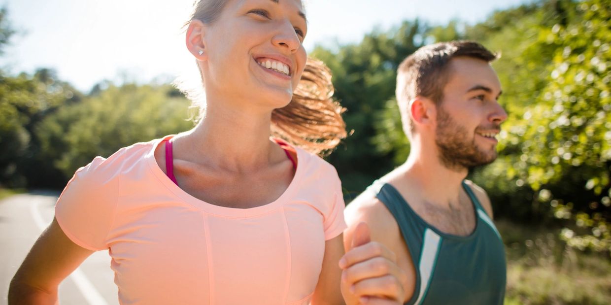 Smiling couple jogging outdoors on a sunny day.