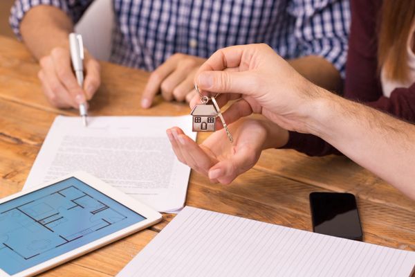 Person holding house key while another signs document.