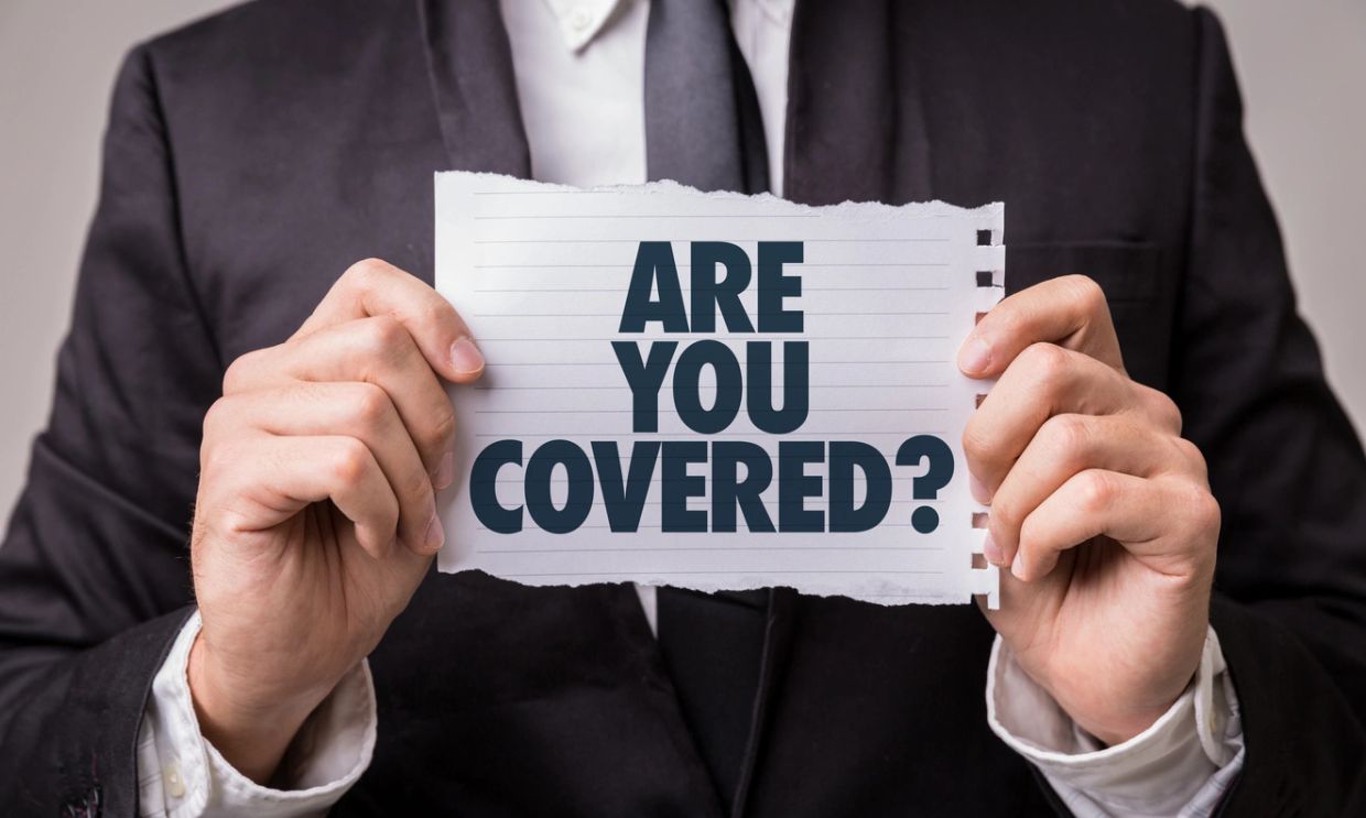 Man in a suit holding a piece of paper that reads, "ARE YOU COVERED?".