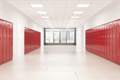 Empty school hallway with red lockers on both sides and large windows at the end.