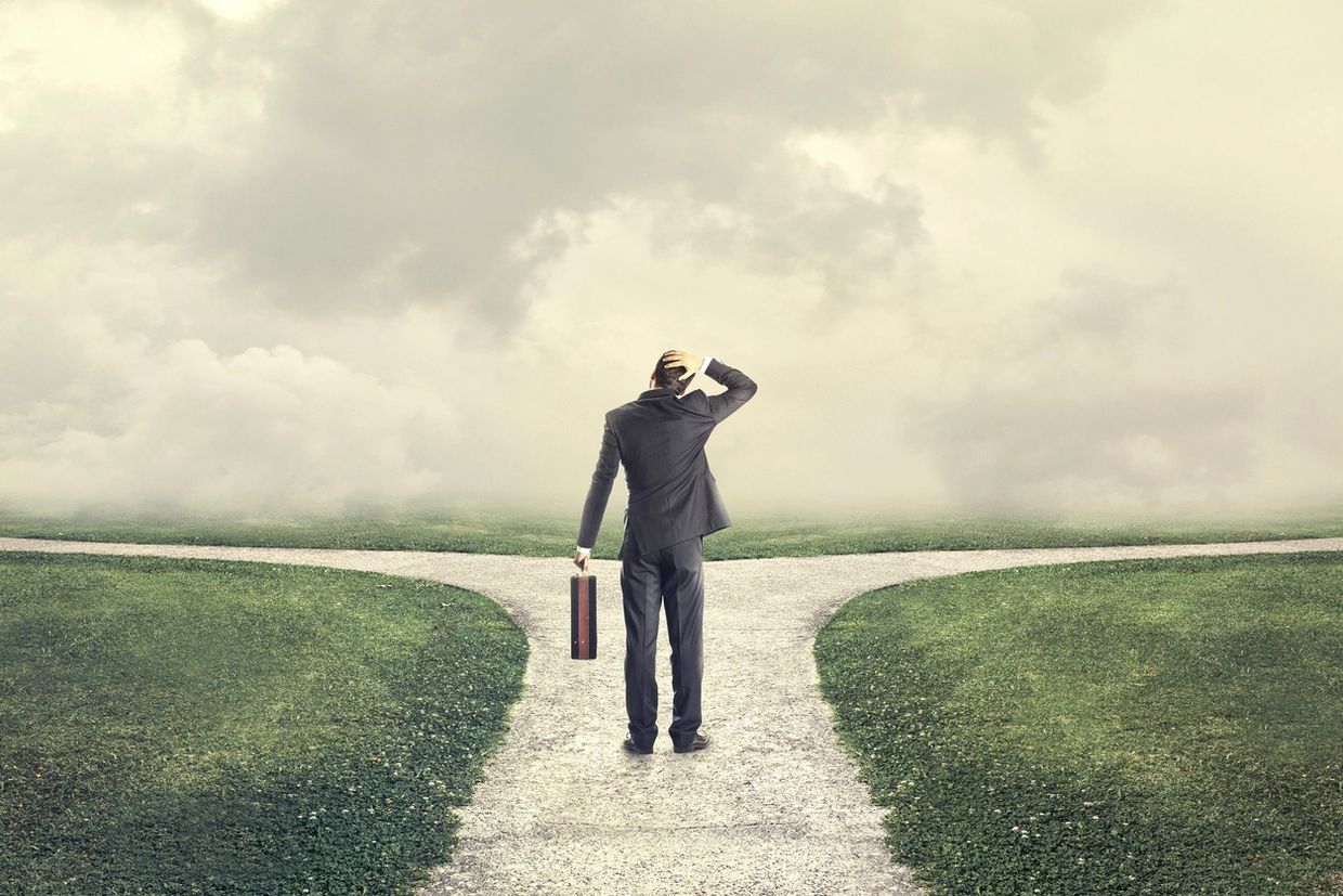 Man in a suit at a forked path, contemplating which way to go.