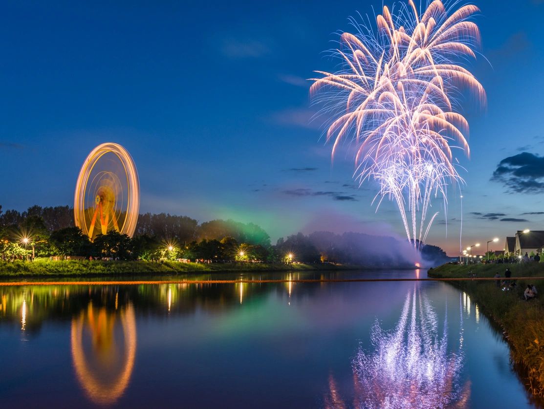Fireworks and a Ferris wheel light up the night by the water.