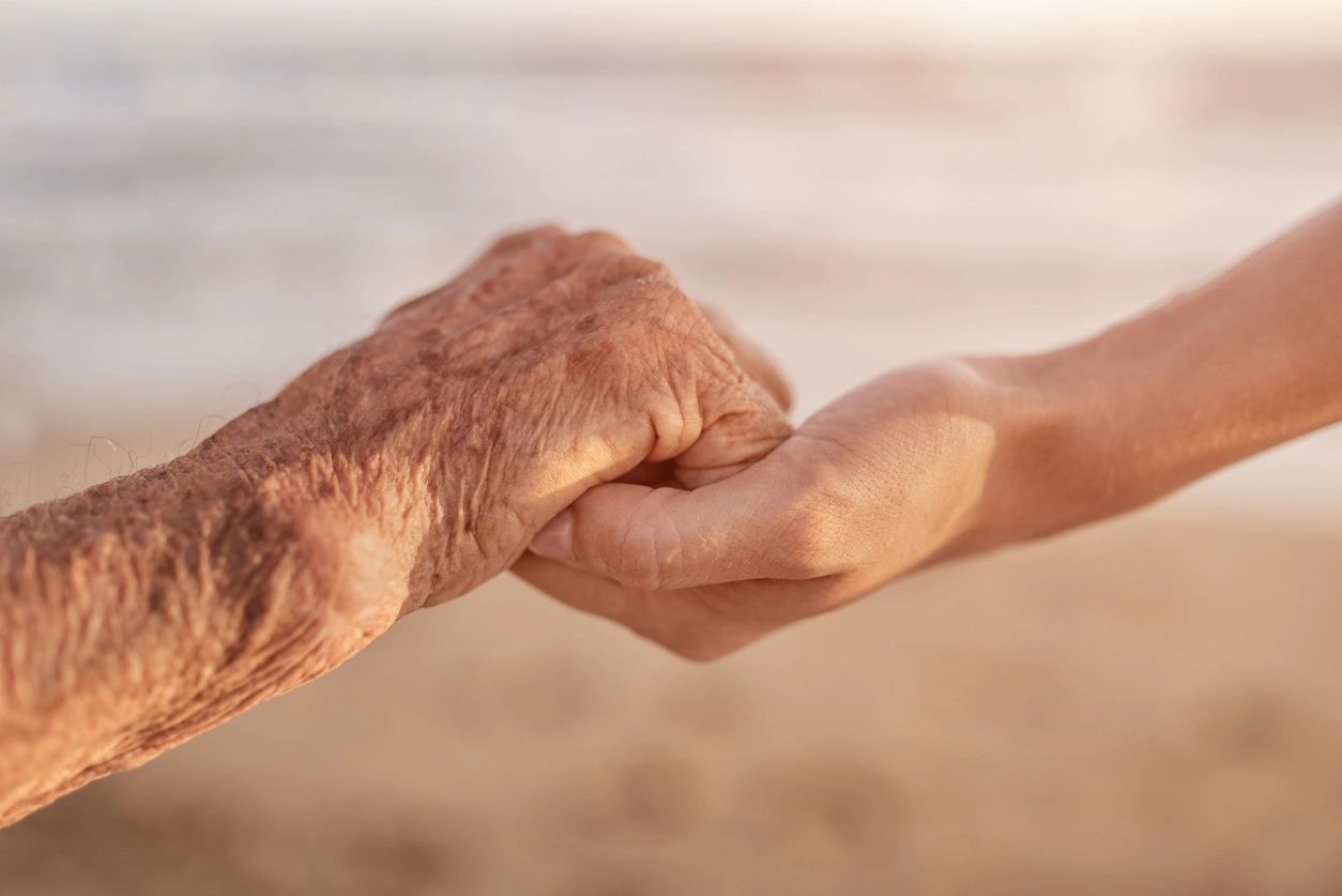 Two people holding hands, one person appears younger, one person older. Shows respect and compassion