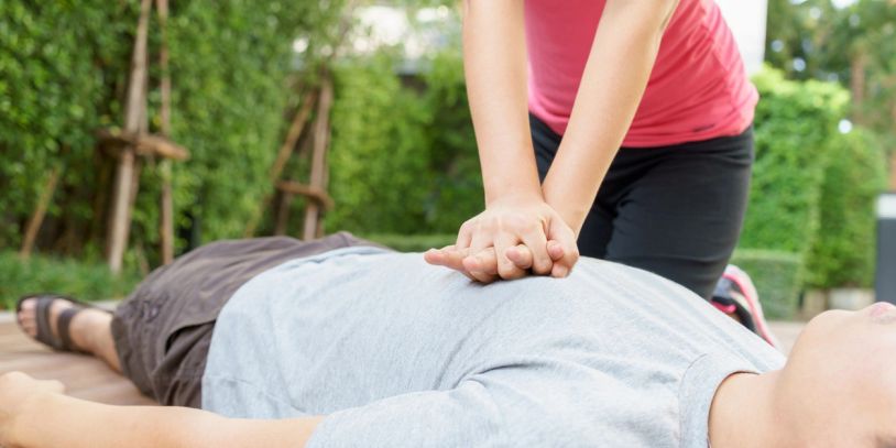 Person performing CPR on an unconscious individual outdoors.