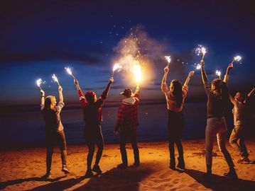 Group of friends holding sparklers at night on a beach.
