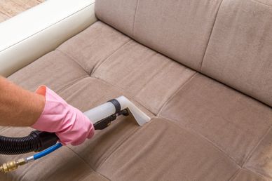 Professional upholstery cleaning technician using extraction equipment to deep clean a tan fabric so