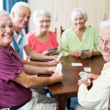 Seniors joyfully playing cards together around a wooden table.