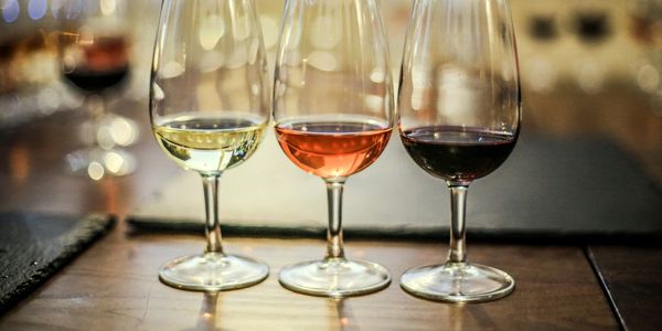 Three wine glasses with white, rosé, and red wine on a wooden table.