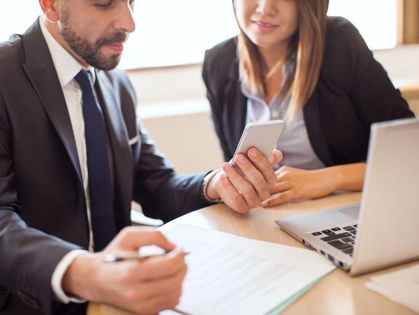 Two professionals discussing documents with a smartphone and laptop.