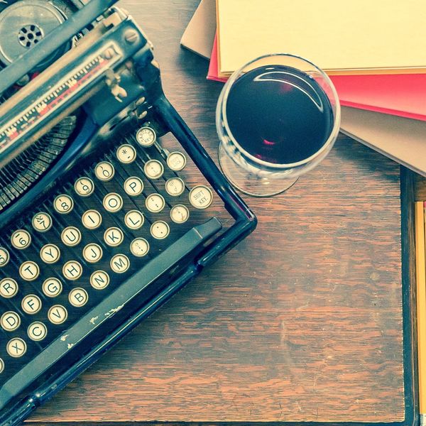 Manual Typewriter on wooden cherry desk with glass of wine and journals and pencils