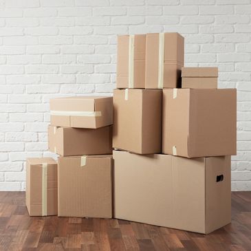 Stack of taped cardboard boxes against a white brick wall.