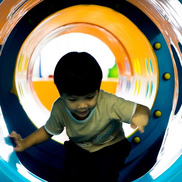 A young boy playing inside a colorful tunnel slide at a playground.