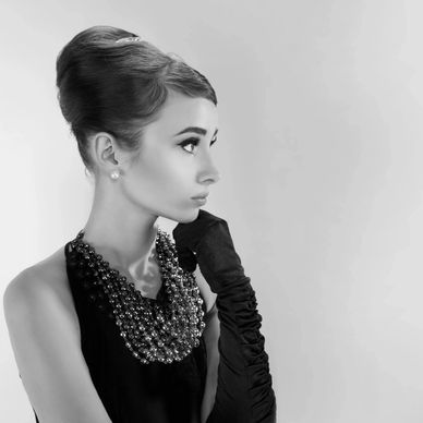 Elegant woman in a classic black dress with gloves and beaded necklace.