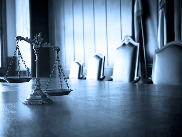 Scales of justice on a wooden table in a dimly lit courtroom.