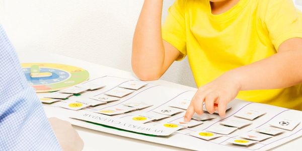 Child in yellow shirt engaging with educational cards at a table.