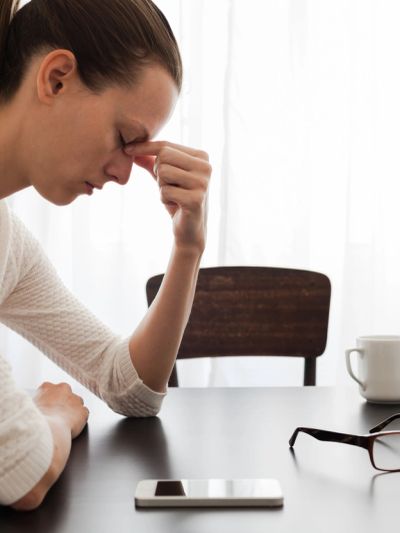 Tired woman sitting at a table with her eyes closed and pinching the bridge of her nose.