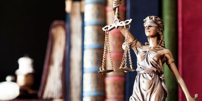 Statue of Lady Justice with legal books blurred in the background.