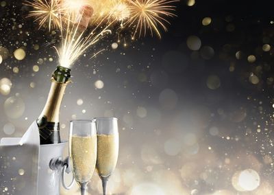 Champagne bottle popping with sparkling fireworks and two filled glasses.