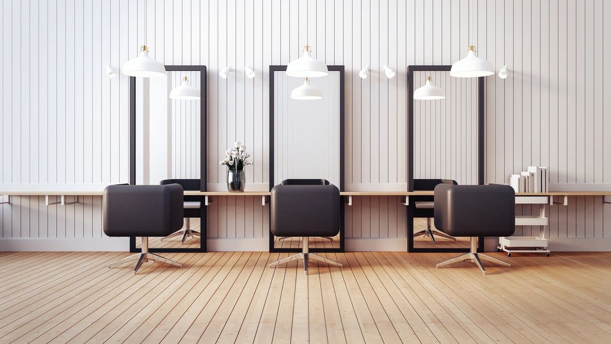 Modern salon setup with three black chairs and large mirrors against a white paneled wall.