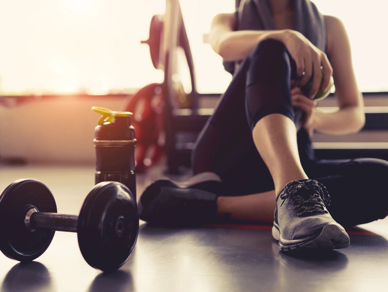 Person resting on the floor after a workout with dumbbell and water bottle nearby.