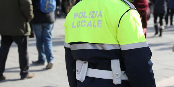 Polizia Locale officer in high-visibility jacket stands in a public area.