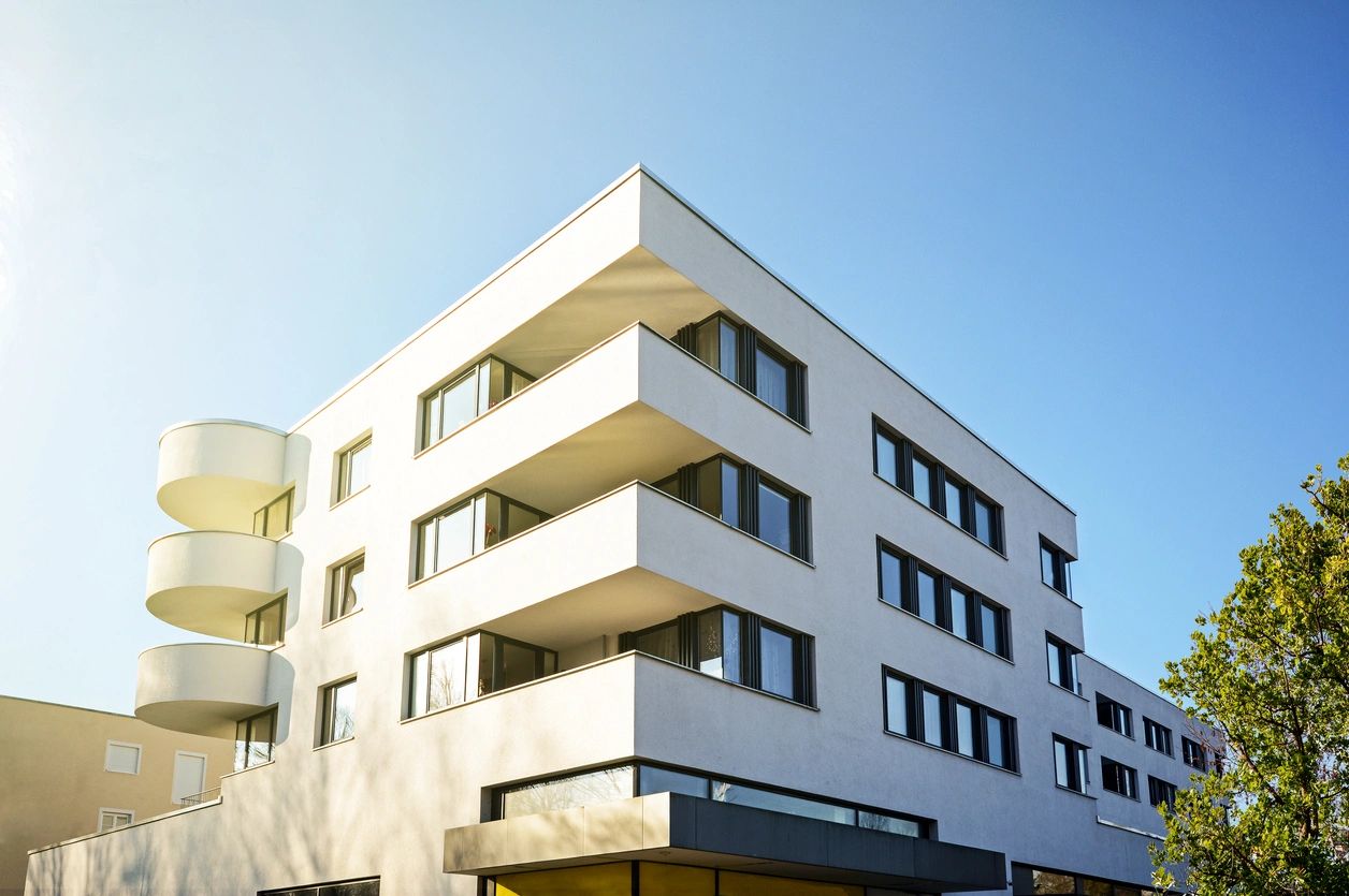 Modern white apartment building with balconies under a clear blue sky.