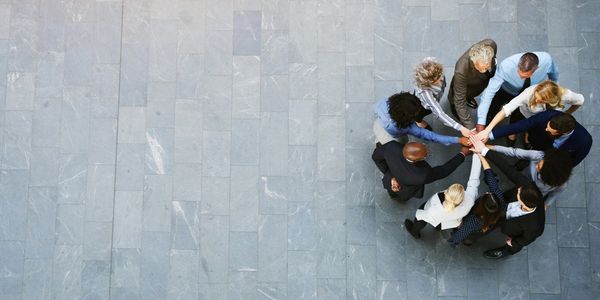 Diverse team standing in a circle, stacking hands in unity.