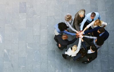Aerial photo of several people standing in a circle with their hands in the middle. 