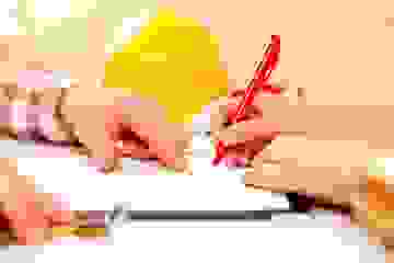 A man pointing out where to sign to a woman holding a red pen, in front of a yellow hard hat.