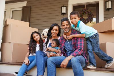 Happy family sitting on porch steps with moving boxes.