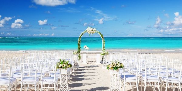 Wedding reception on a beach with chairs and a wedding arch.