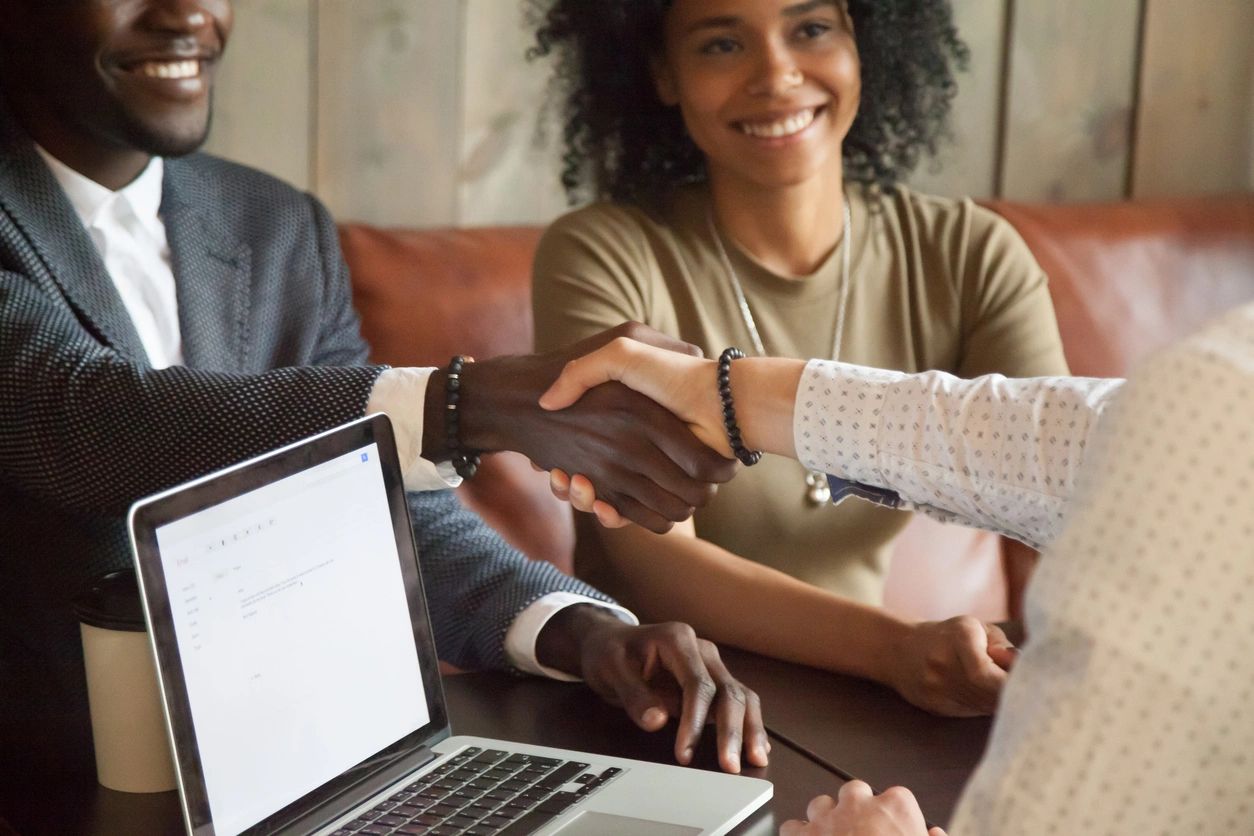 Clients shaking hands with an agent over a computer 