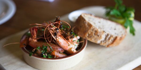 A bowl of cooked shrimp garnished with herbs, served with a slice of bread.