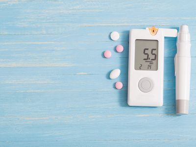 Blood glucose meter showing 5.5 with pills on a blue wooden surface.