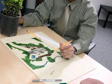 A man draws a landscape design with plants and paving stones.