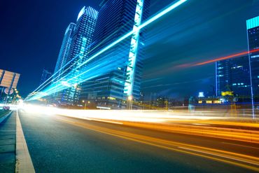 Night cityscape with light trails from fast-moving traffic and illuminated skyscrapers.
