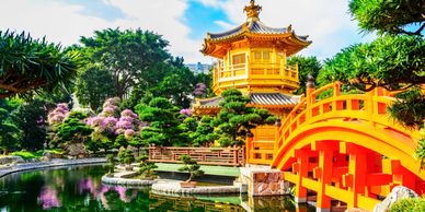A vibrant Asian garden with a golden pavilion and red arched bridge over water.