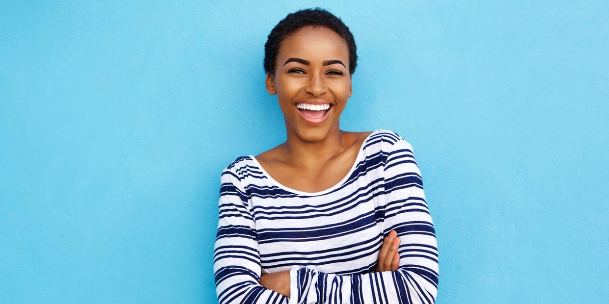 A joyful young woman smiling confidently against a blue background.