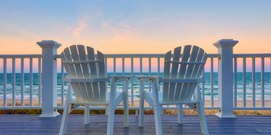 Adirondack chairs on a deck at the beach at sunset.  