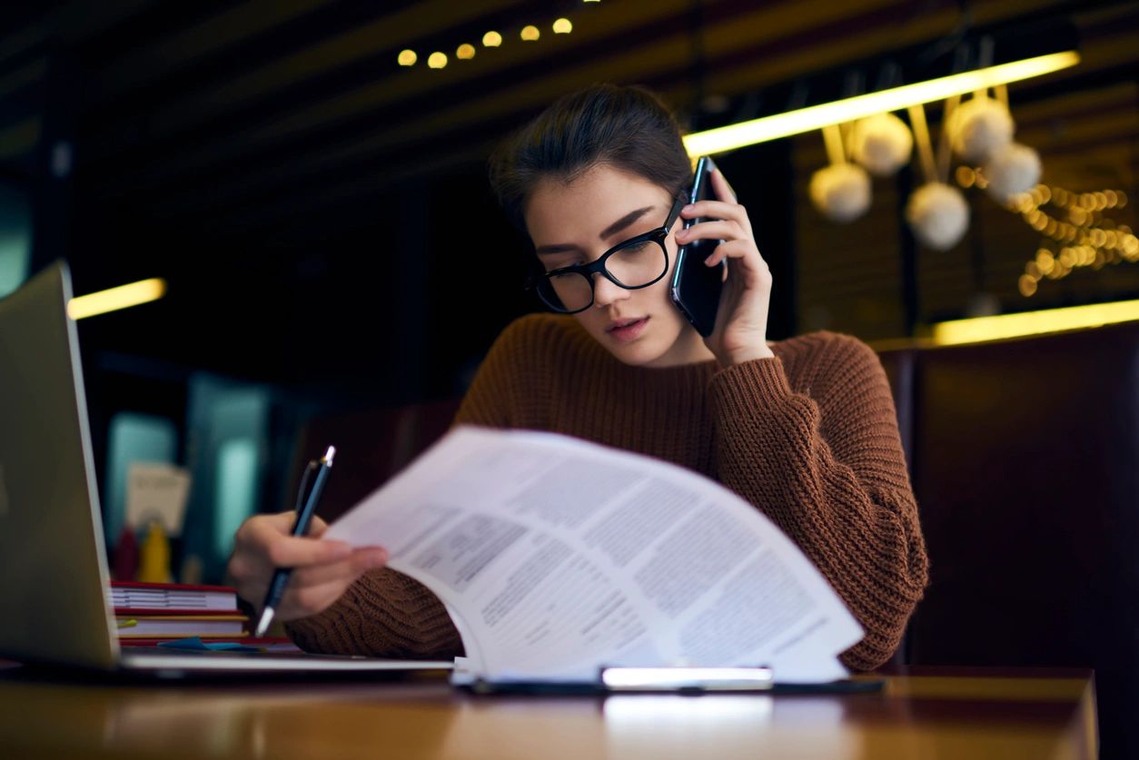 A young lady shares her feedback from the notes she has, on a phone call, with her laptop in front of her.